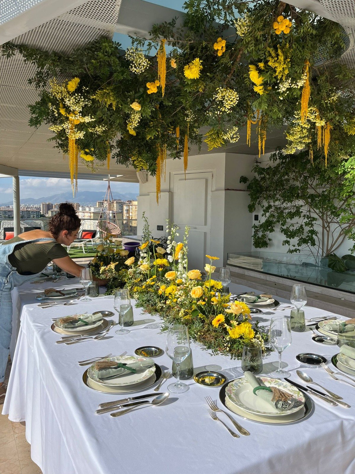 Mesa de evento con decoración floral amarilla y vegetación suspendida